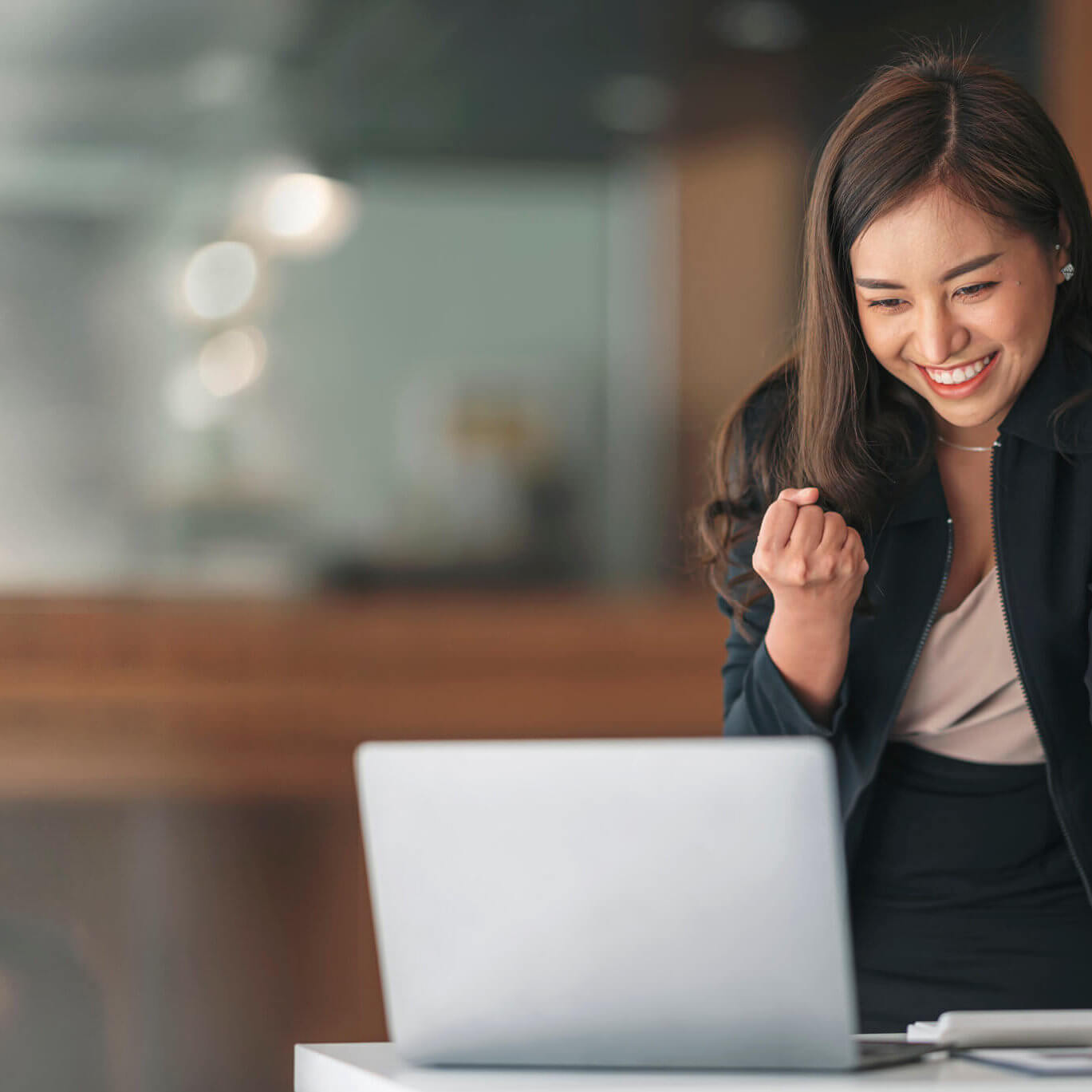 Young successful businesswoman raising her hands up and laughing with happiness.